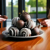 Stacked dark chocolate truffles with white drizzle from the Delight Chocolate Box - Gourmet Gift, served on a plate for sharing.